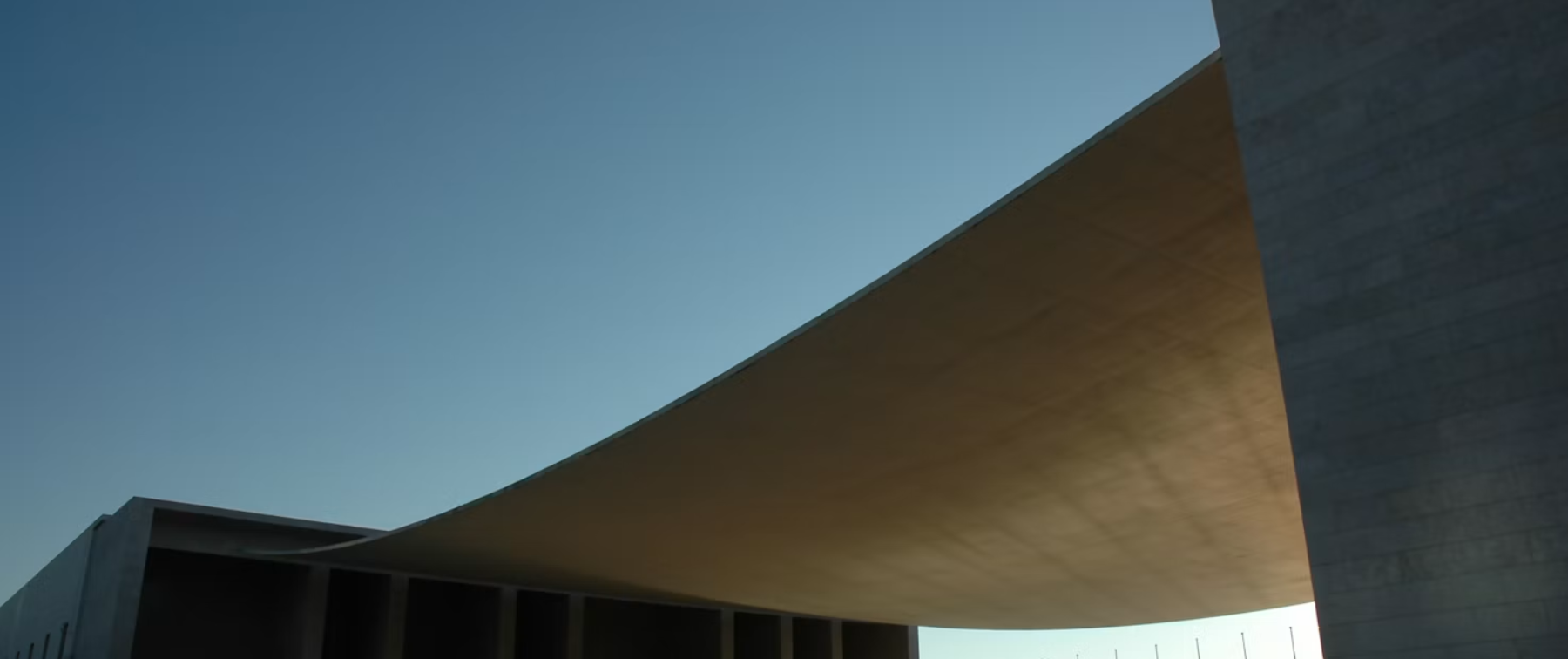 A concrete canopy curving over an open plaza at dusk